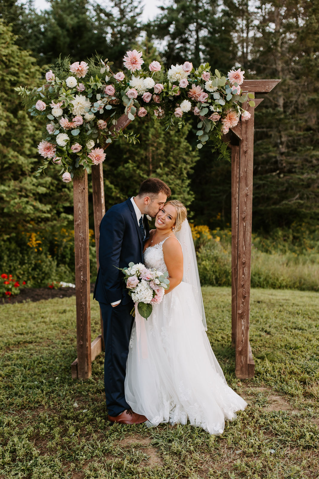 Bride and groom under the floral arbor in the meadow at Sunset Meadows